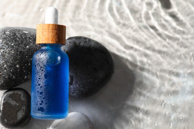 Photo of Bottle of face serum and spa stones in water on light background, closeup. Space for text