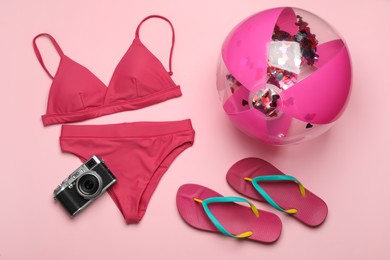 Photo of Beach ball, swimsuit, flip flops and camera on pink background, flat lay
