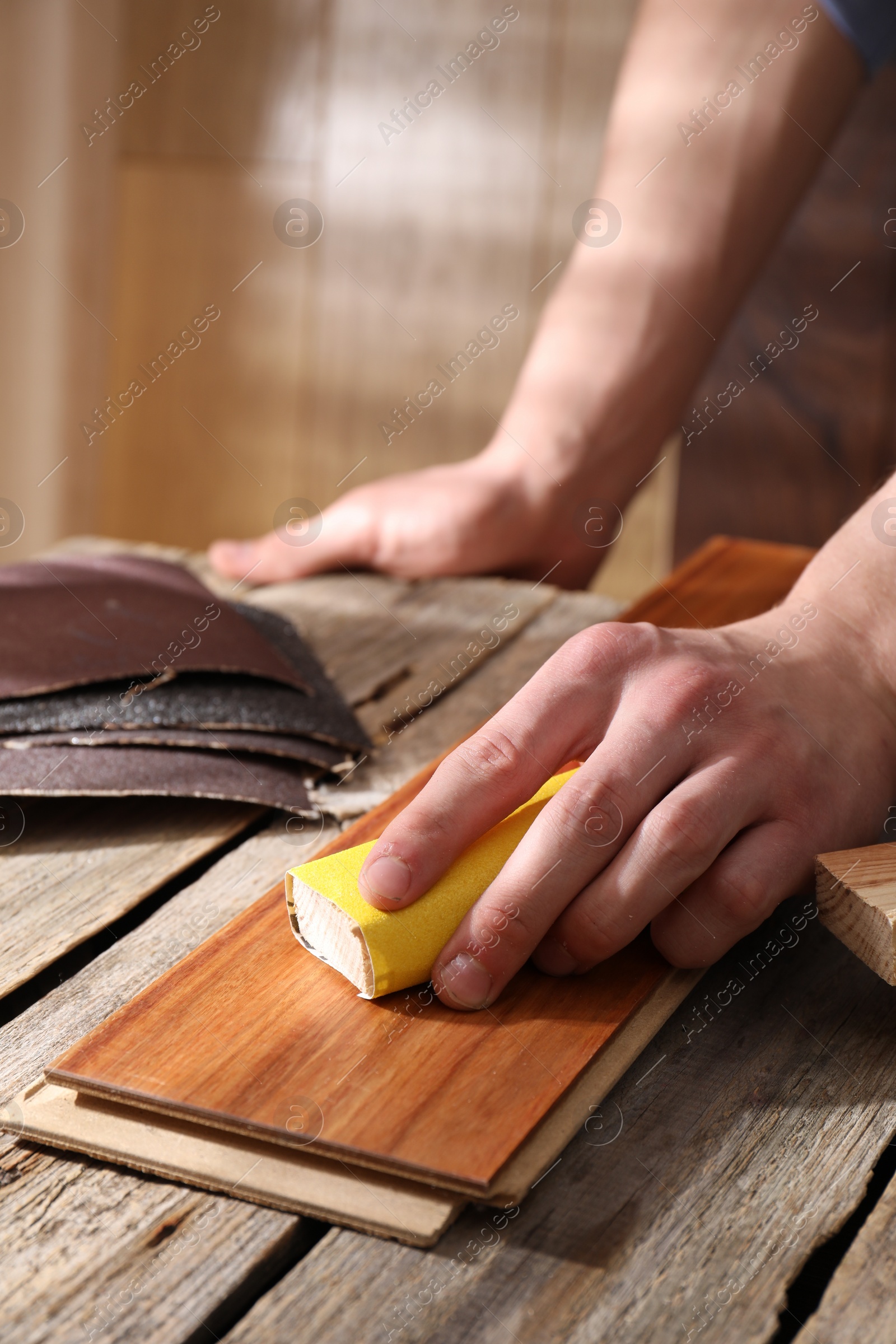 Photo of Man polishing wooden plank with sandpaper at table indoors, closeup