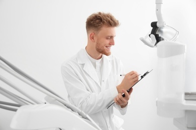 Photo of Professional male dentist with clipboard in clinic