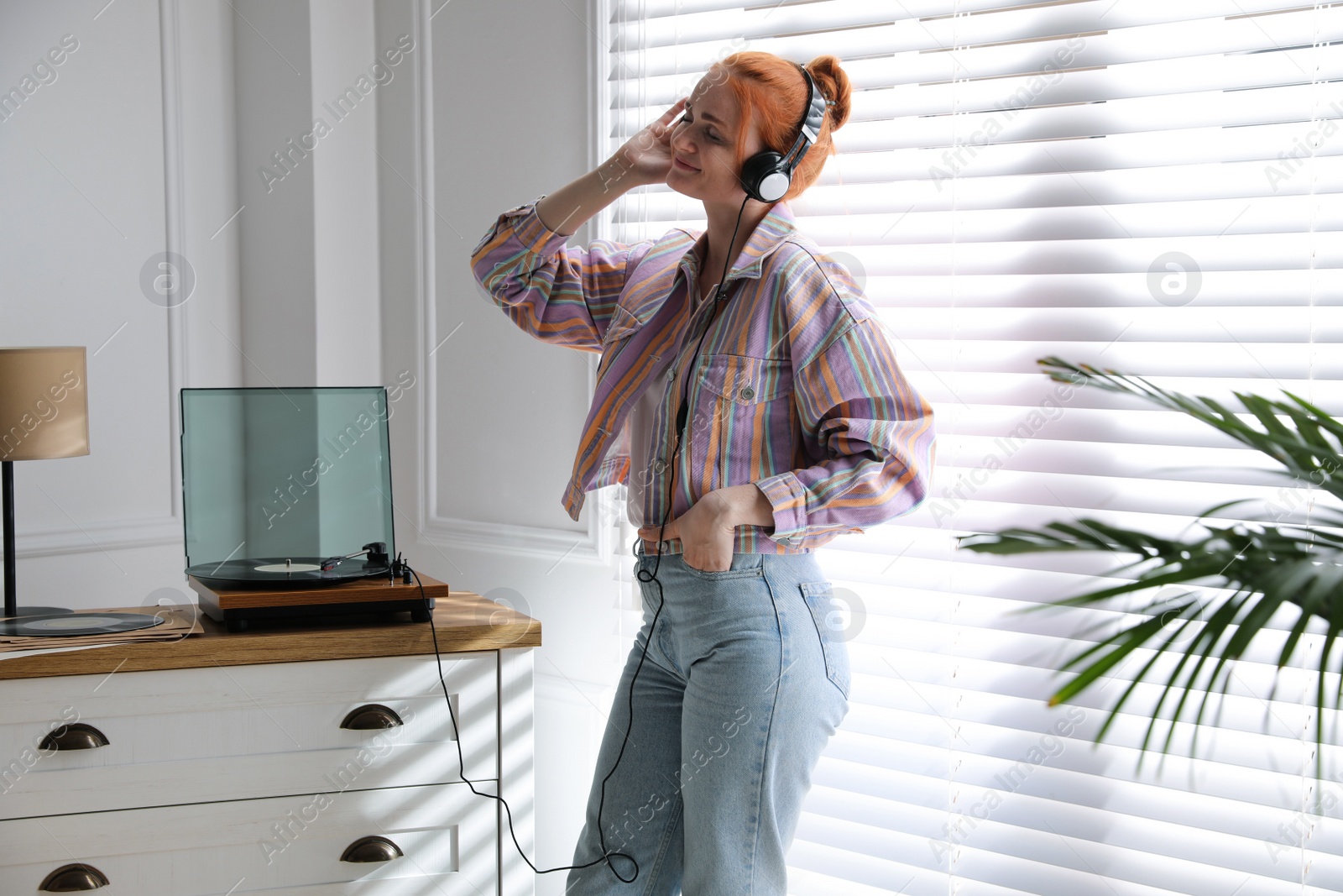 Photo of Young woman listening to music with turntable at home