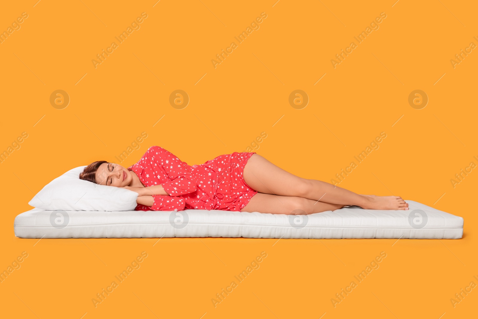 Photo of Young woman sleeping on soft mattress against orange background