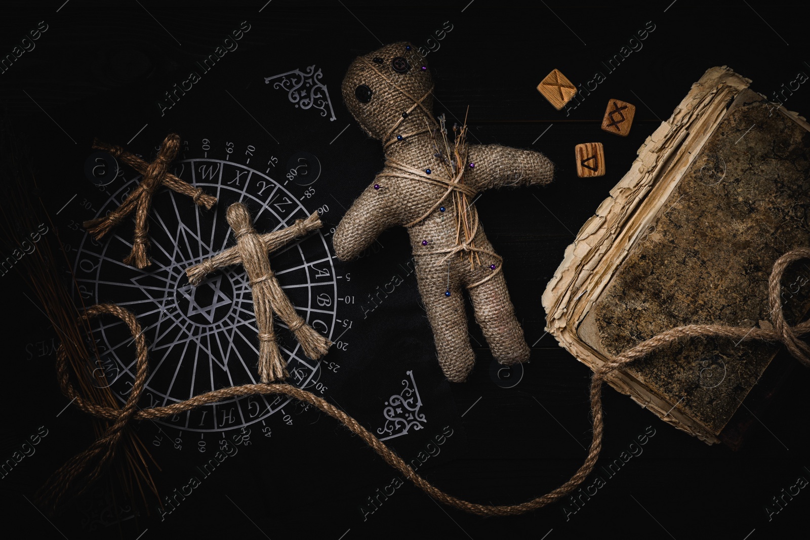 Image of Voodoo doll with pins surrounded by ceremonial items on table, flat lay