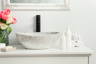 Photo of Vase with beautiful pink tulips and toiletries near sink in bathroom