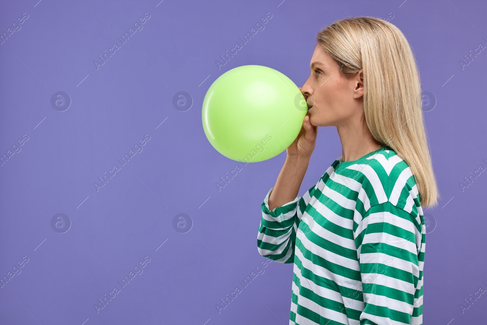 Photo of Woman blowing up balloon on violet background. Space for text