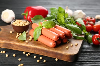 Fresh raw vegetarian sausages with basil, soybeans and vegetables on black wooden table