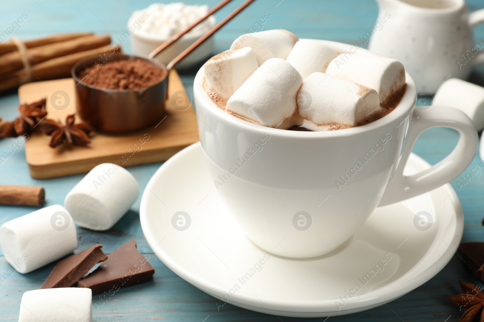 Photo of Tasty hot chocolate with marshmallows and ingredients on light blue wooden table, closeup