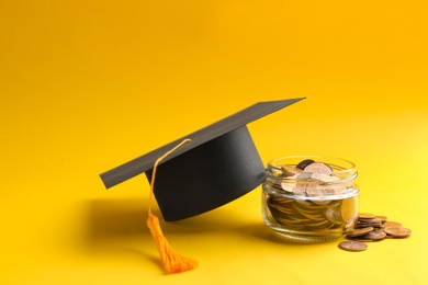 Photo of Glass jar, coins and graduation hat on color background. Space for text