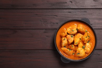 Photo of Delicious chicken curry in pan on wooden table, top view. Space for text