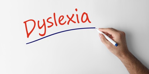 Man writing word Dyslexia on white background, closeup. Banner design