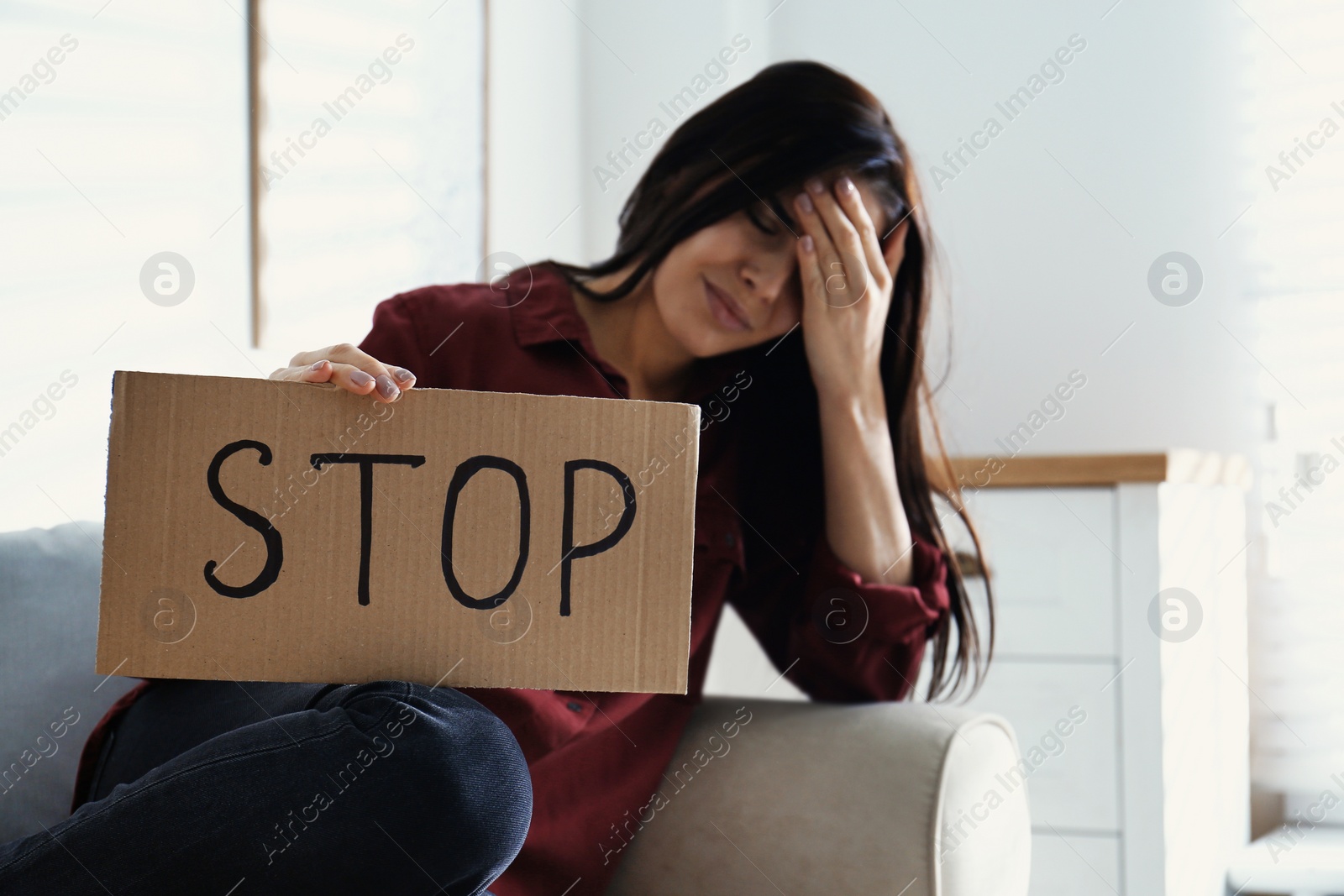 Photo of Crying young woman with sign STOP indoors. Domestic violence concept