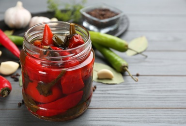 Photo of Glass jar of pickled chili peppers on grey wooden table, closeup. Space for text