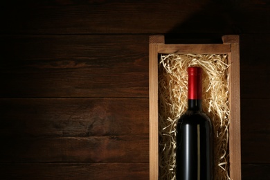 Photo of Crate with bottle of wine on wooden table, top view. Space for text