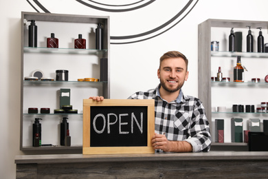 Young business owner holding OPEN sign in his barber shop