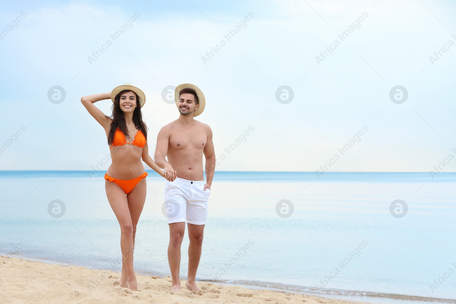 Photo of Happy young couple in hats walking together on beach. Space for text