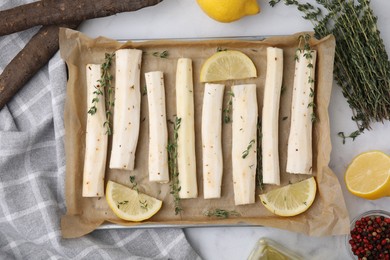 Photo of Baking tray with raw salsify roots, lemon and thyme on white marble table, flat lay