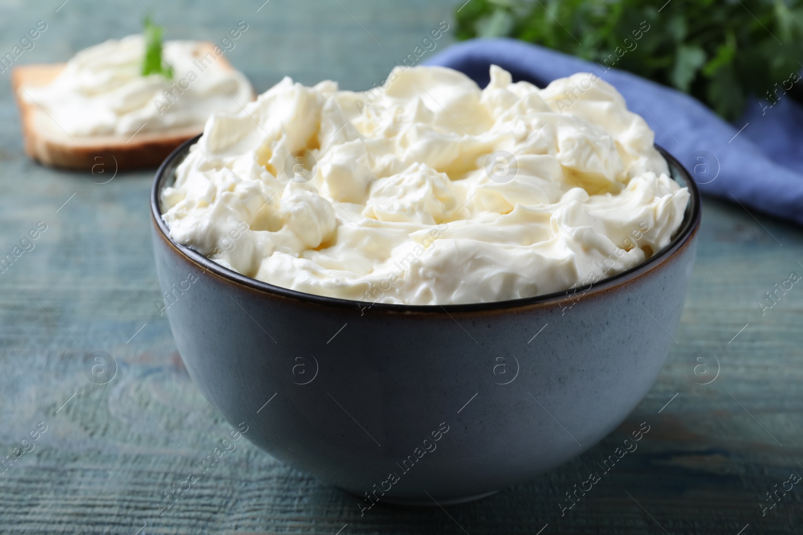 Photo of Tasty cream cheese on light blue wooden table, closeup