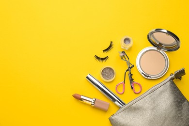 Eyelash curler, cosmetic bag and makeup products on yellow background, flat lay. Space for text