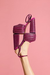Woman wearing high heeled shoe with platform and square toes holding another one on pink background, closeup. Stylish presentation
