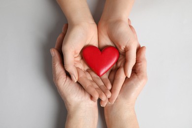 Photo of Young and elderly women holding red heart on light grey background, top view