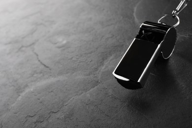 Photo of Referee equipment. Metal whistle on black textured background, closeup and space for text