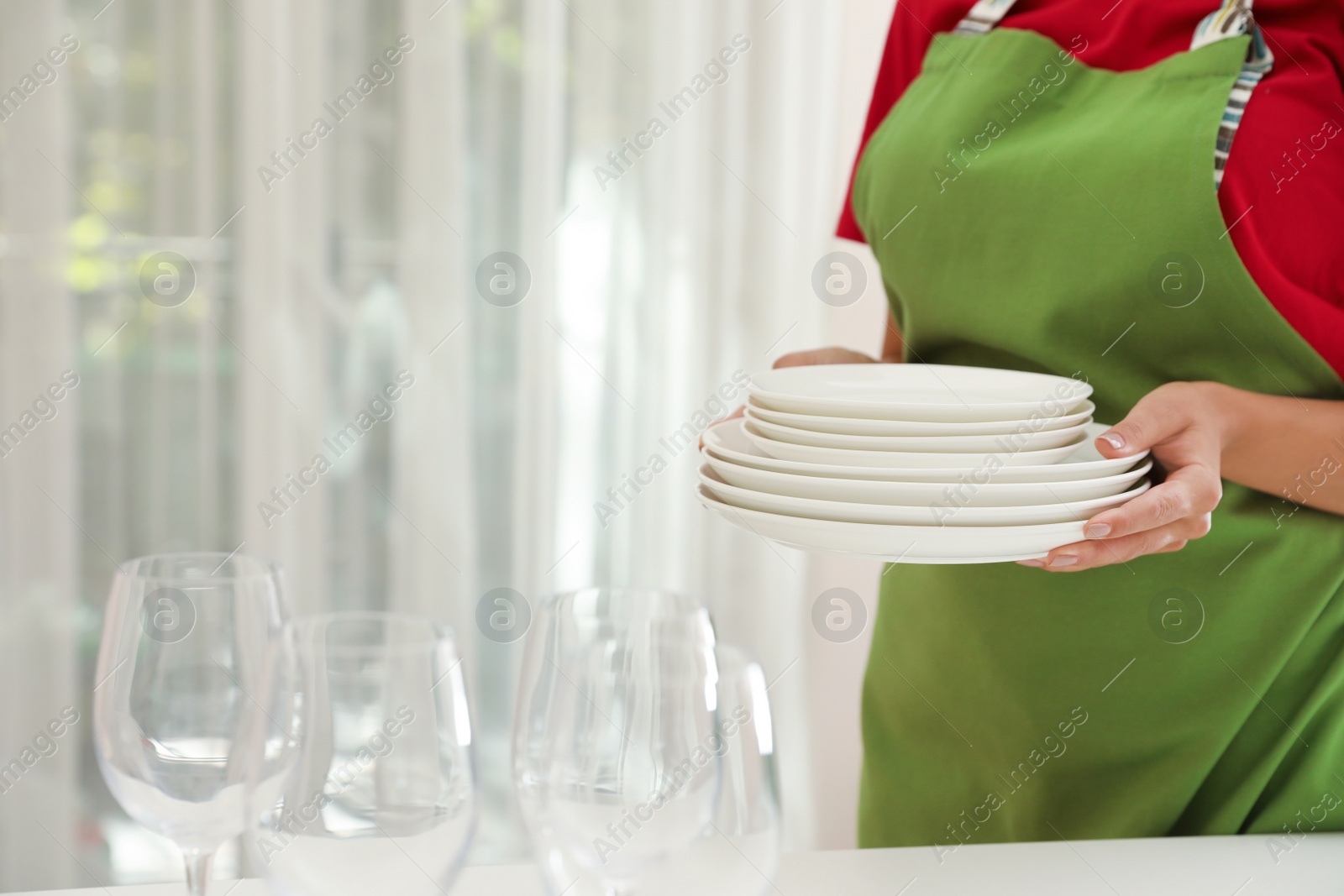 Photo of Woman holding stack of clean dishes indoors, closeup. Space for text