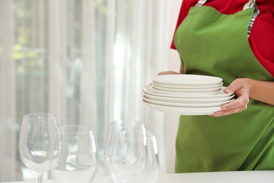 Woman holding stack of clean dishes indoors, closeup. Space for text