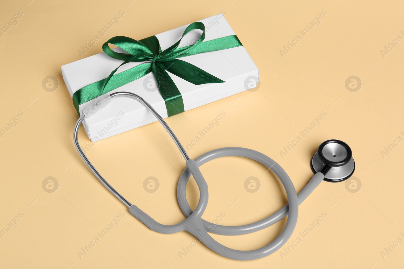 Photo of Stethoscope and gift box on beige background. Happy Doctor's Day