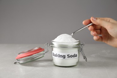 Photo of Woman taking baking soda with spoon from jar at grey table, closeup