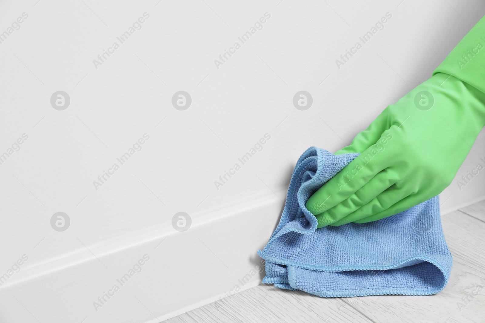 Photo of Woman in gloves cleaning plinth with cloth indoors, closeup. Space for text