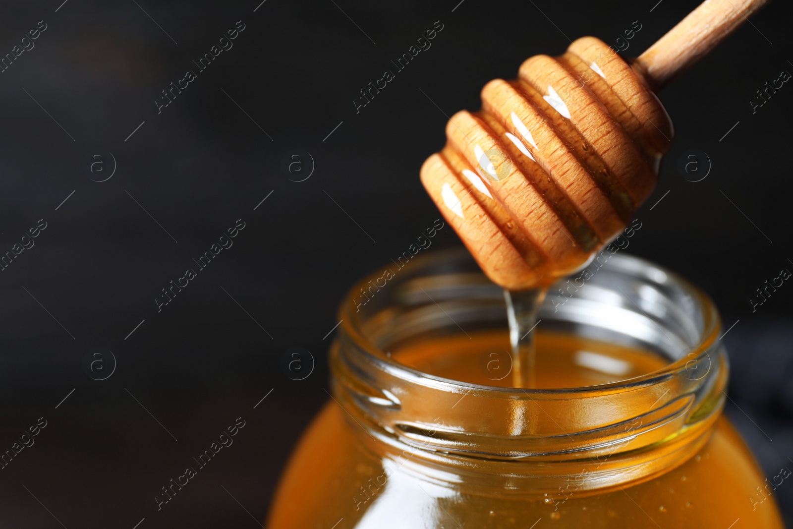 Photo of Jar of organic honey and dipper on dark background, closeup