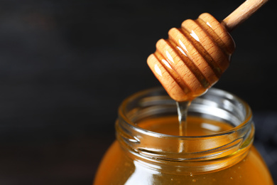 Jar of organic honey and dipper on dark background, closeup