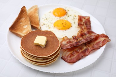 Tasty pancakes with fried eggs and bacon on white tiled table
