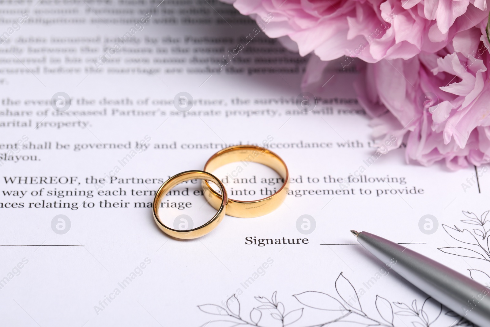 Photo of Marriage contract, golden wedding rings, pen and flowers, closeup