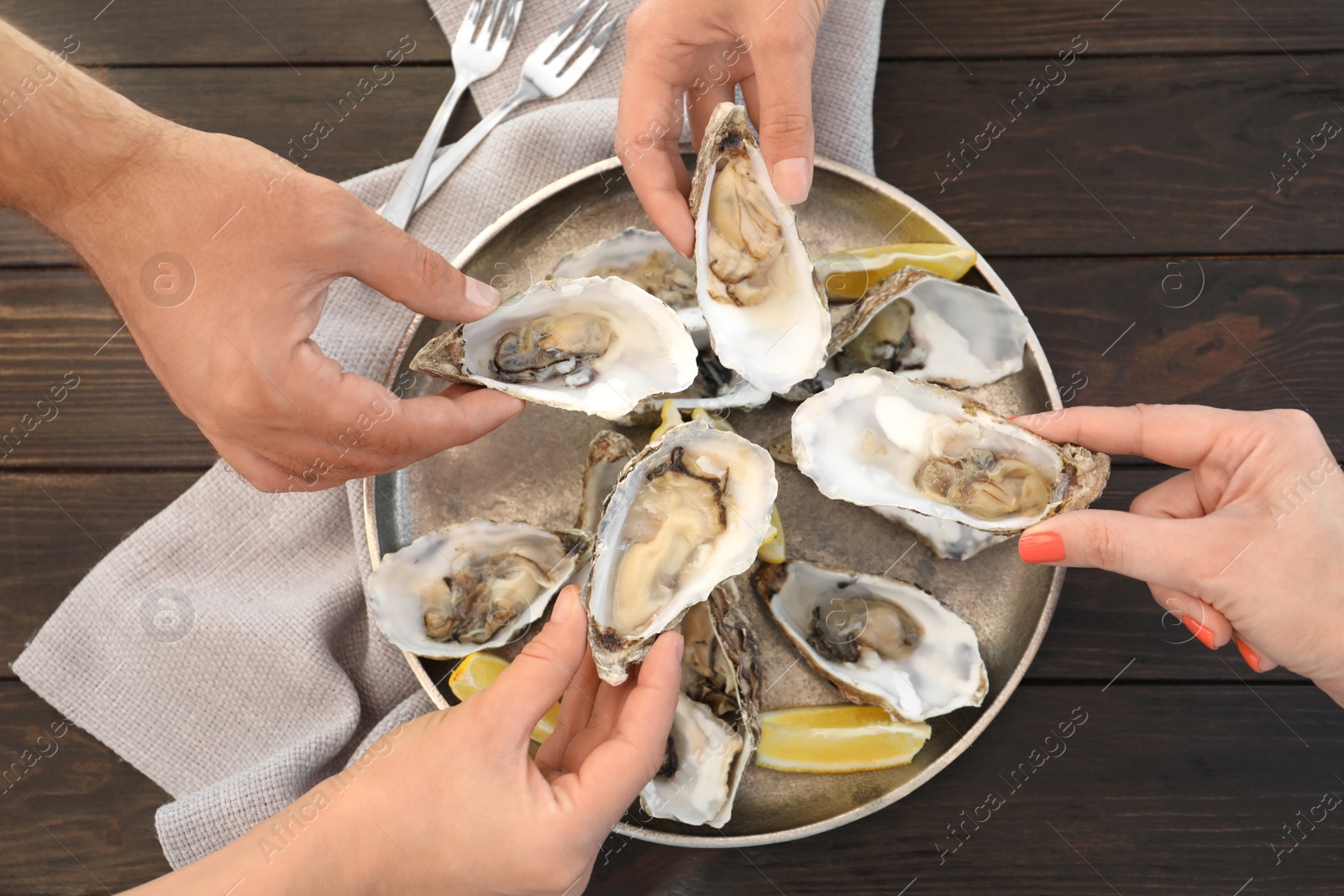 Photo of Top view of people with fresh oysters at table, focus on hands