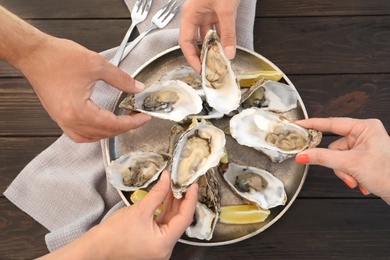 Photo of Top view of people with fresh oysters at table, focus on hands