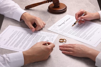 Man and woman signing marriage contract at light grey table, closeup