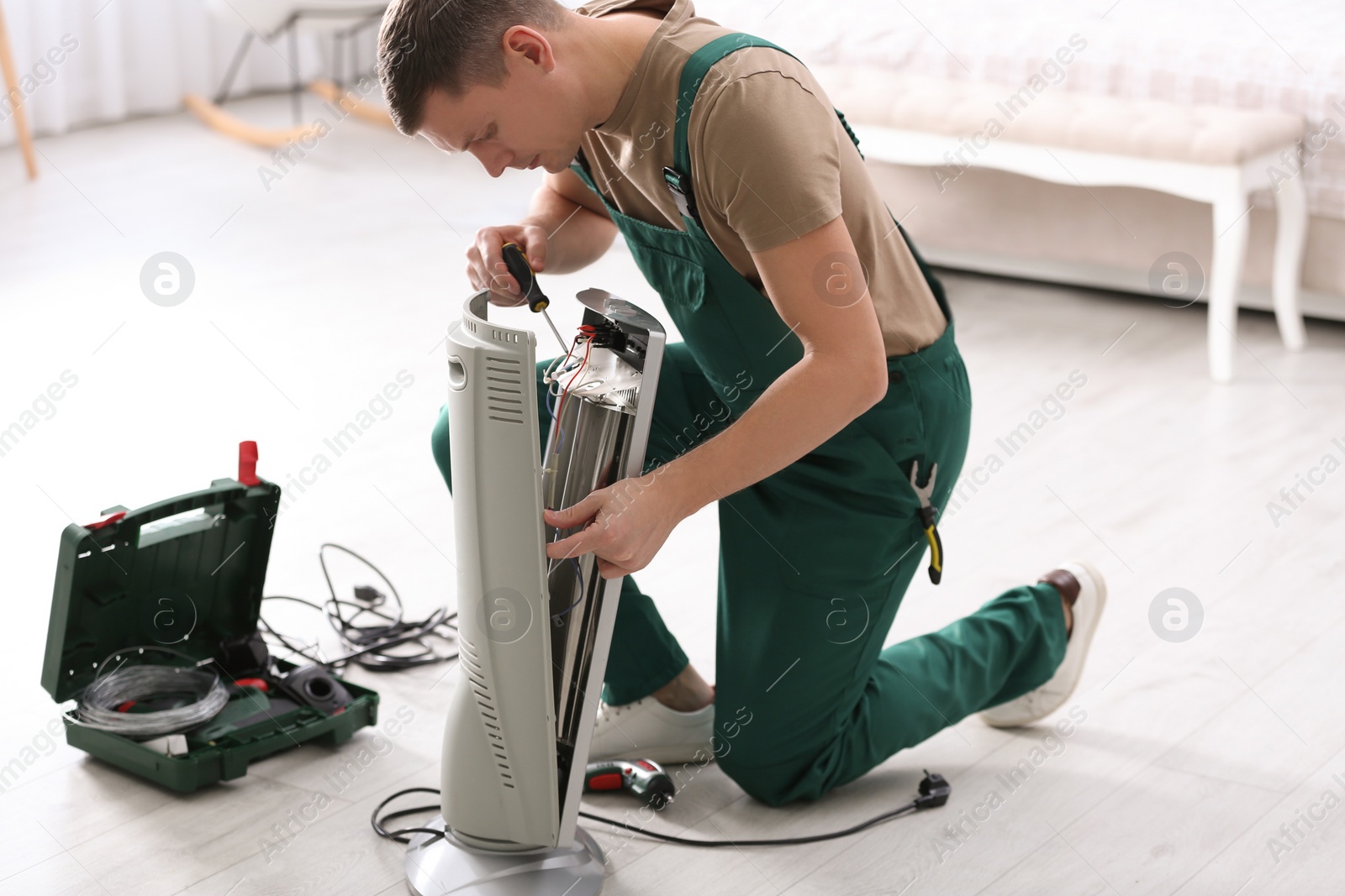 Photo of Professional technician repairing electric ultrared heater with screwdriver indoors