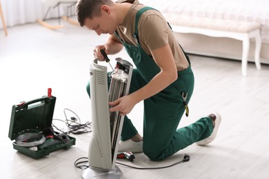 Professional technician repairing electric ultrared heater with screwdriver indoors