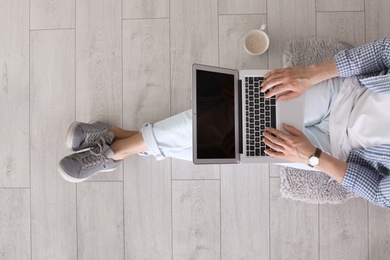 Photo of Young man with laptop sitting on floor, top view