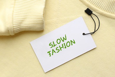 Image of Conscious consumption. Tag with words Slow Fashion on yellow sweatshirt, top view