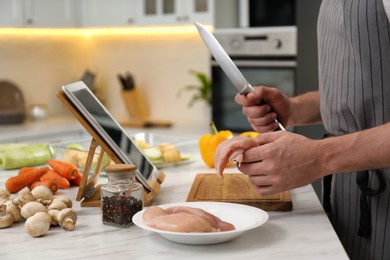 Photo of Man making dinner while watching online cooking course via tablet in kitchen, closeup