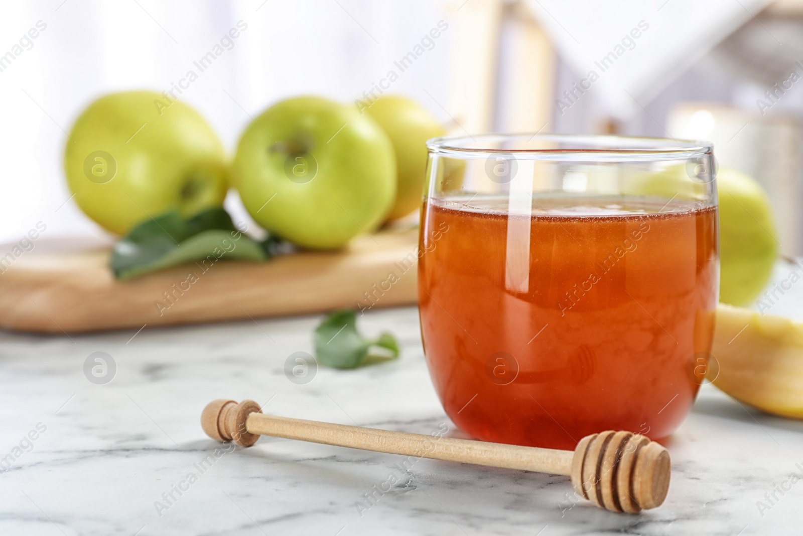 Photo of Glass of honey, apples and dipper on marble table