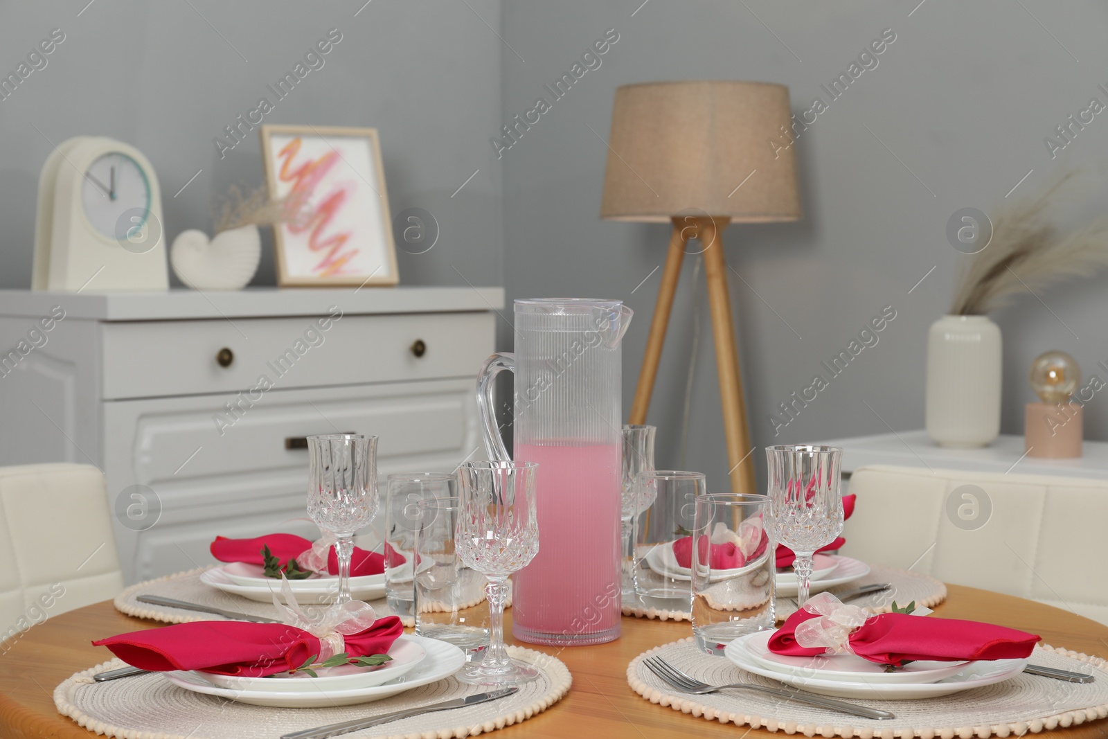 Photo of Color accent table setting. Glasses, plates, jug of beverage and pink napkins in dining room