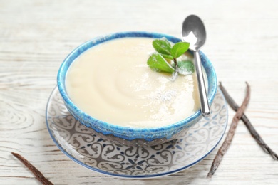 Photo of Vanilla pudding, sticks and fresh mint on wooden background