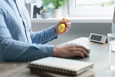 Man squeezing antistress ball while working in office, closeup