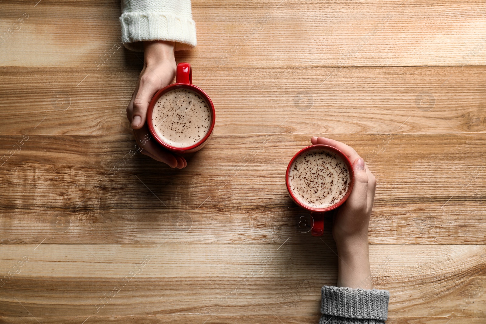 Photo of Women with cups of coffee at wooden table, top view