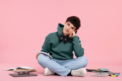 Portrait of student with notebook and stationery sitting on pink background