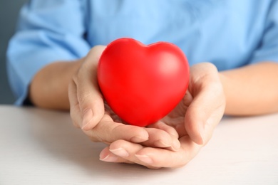 Photo of Doctor holding red heart at wooden table, closeup. Cardiology concept