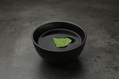 Photo of Black bowl with water and green leaf on grey table